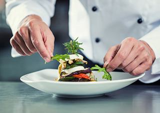 Un chef dresse artistiquement un plat gourmet avec des ingrédients frais sur une assiette blanche | MSC Cruises