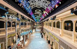 A vibrant and spacious interior view of the Galleria on MSC Virtuosa, showcasing shops and entertainment | MSC Cruises