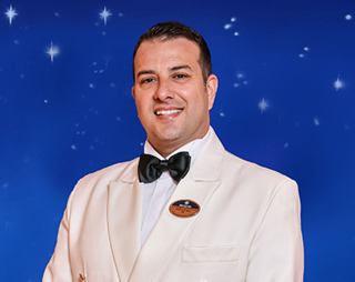 Captain Giovanni Guarracino smiles warmly, dressed in a formal white suit against a starry blue backdrop | MSC Cruises