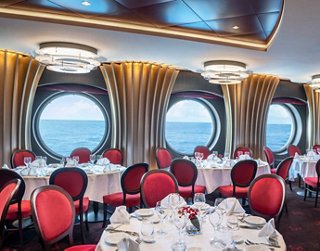 Elegant restaurant featuring red chairs and round windows offering a sea view | MSC Cruises