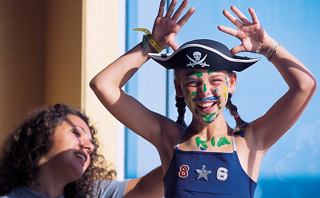 A child in a pirate hat joyfully plays with face paint while a friend laughs nearby | MSC Cruises