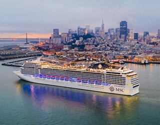 Un magnifique paquebot illuminé au crépuscule, avec une skyline urbaine vibrante en arrière-plan | MSC Cruises