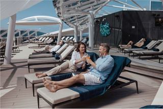Two people relaxing on loungers by the pool on the sun deck of a cruise ship | MSC Cruises