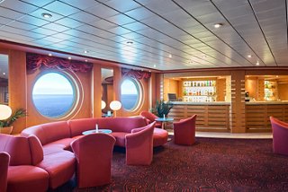 Lounge area with cozy seating and large portholes offering views of the sea | MSC Cruises