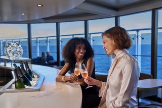 Two women share a drink at a bar overlooking the sea and sky at sunset | MSC Cruises