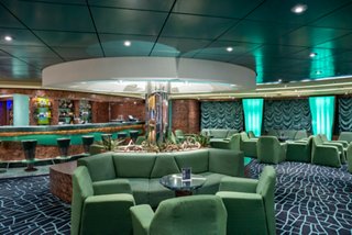 Spacious lounge featuring green armchairs and a central bar area on a cruise ship | MSC Cruises