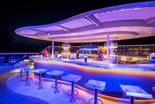 Outdoor bar with vibrant lighting and seating on a cruise ship at night | MSC Cruises