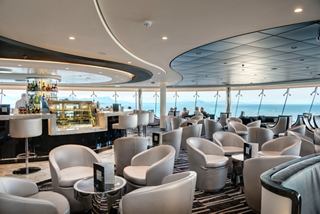 Spacious lounge with large windows, tables and a bar overlooking the sea | MSC Cruises