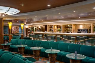 Spacious bar with inviting green armchairs and a sleek counter aboard MSC Orchestra | MSC Cruises