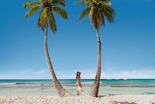 A woman stands between two palm trees on a sandy beach by turquoise waters on Saona Island | MSC Cruises