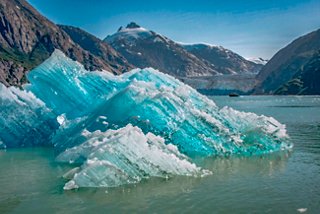 Blue iceberg floats in calm water with mountain scenery in Alaska | MSC Cruises