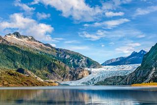 Alaskan glacier and lake surrounded by mountains and a sky with clouds | MSC Cruises