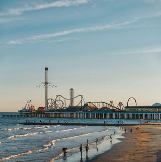 Waves roll onto the sandy beach near a lively pier with an amusement park | MSC Cruises