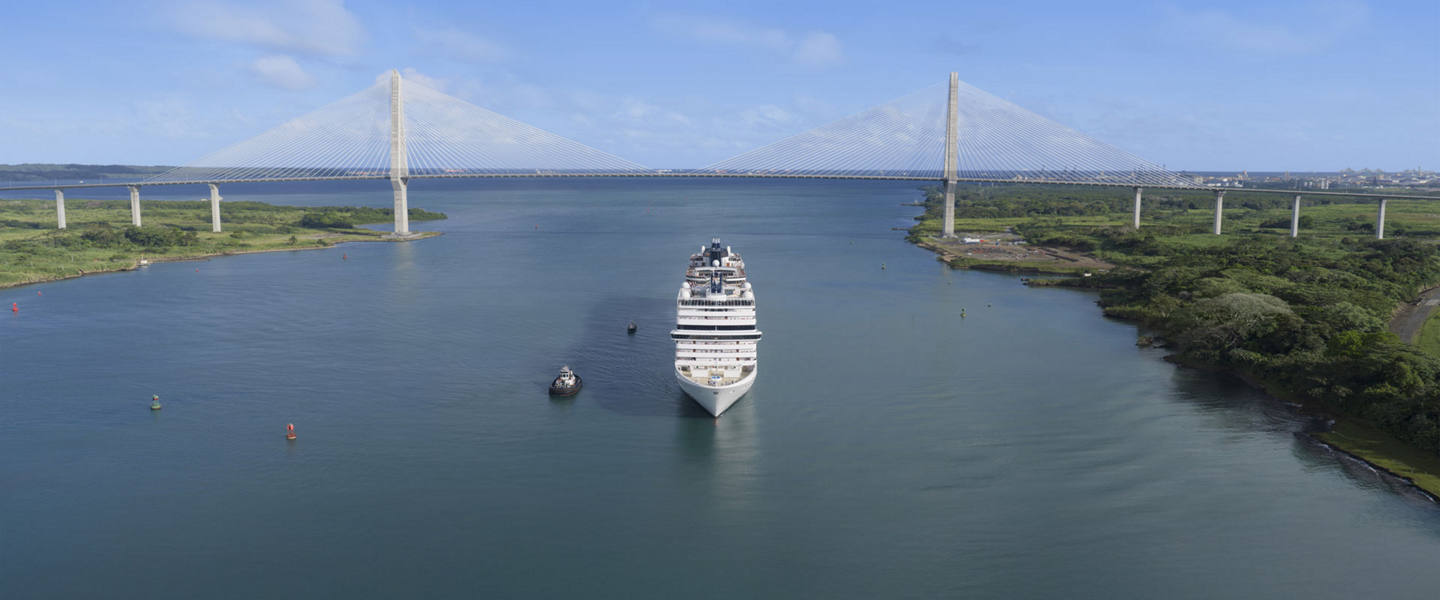 A cruise ship sails through a canal with bridges and lush green banks | MSC Cruises