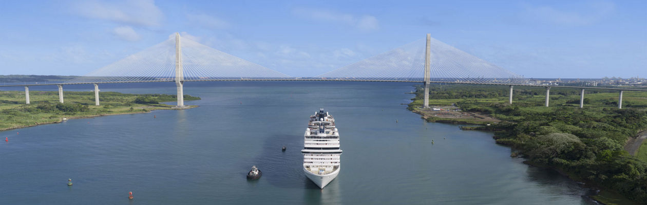 A cruise ship sails through a canal with bridges and lush green banks | MSC Cruises