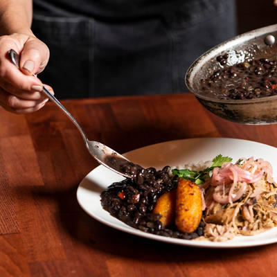 Chef plating a gourmet dish with rice, beans and vegetables on a wooden table | MSC Cruises