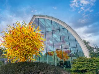 Glass garden with a vibrant sculpture and a modern building under a blue sky | MSC Cruises
