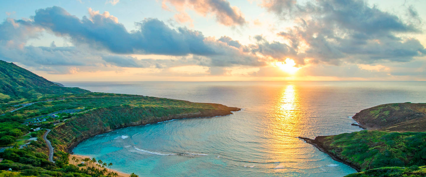 Sunrise shines over a bay surrounded by lush vegetation and calm waters | MSC Cruises