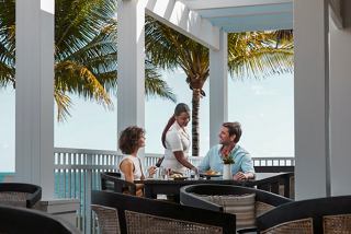 Guests enjoy attentive service at a table in a restaurant overlooking the sea and palm trees | MSC Cruises