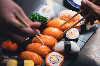 Sushi is arranged on a black platter as hands use chopsticks to select pieces | MSC Cruises