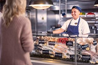 A woman interacts with crew behind the seafood counter at La Pescaderia on MSC Cruises | MSC Cruises