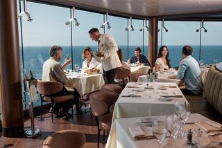 Guests enjoy lunch by glass walls overlooking the sea and sky in a vibrant restaurant setting | MSC Cruises