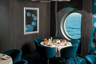 A beautifully set dining table beside a round window overlooking the sea | MSC Cruises