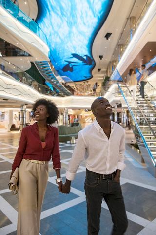 A couple strolls under the vibrant LED sky screen in the World Galleria on MSC World Europa | MSC Cruises