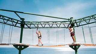 Guests cross a rope bridge above the sea beneath a bright sky | MSC Cruises
