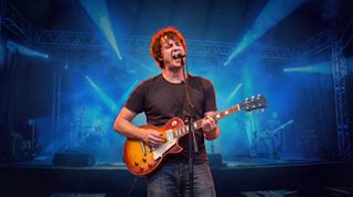 A man plays guitar on stage with inspiring blue lights in the background | MSC Cruises