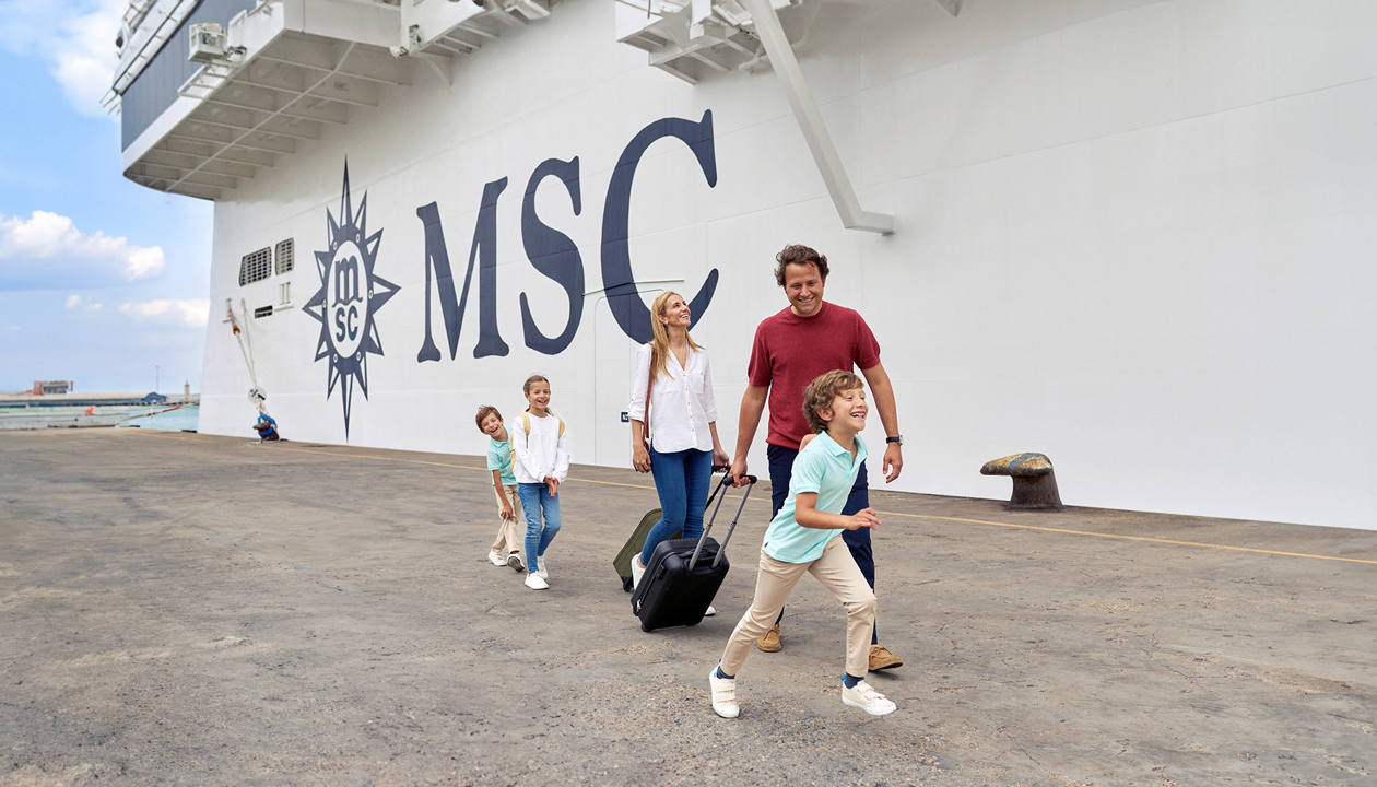 A family with young children and luggage walks together beside an MSC Cruises ship | MSC Cruises