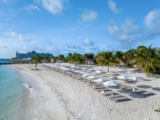 Sun loungers and umbrellas line a sandy beach beside turquoise water and lush greenery | MSC Cruises