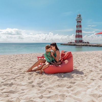 A family relaxes on the sandy beach with a lighthouse and clear blue sky | MSC Cruises