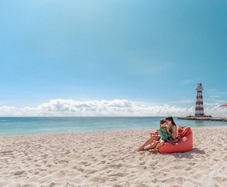 A family relaxes on the sandy beach with a lighthouse and clear blue sky | MSC Cruises