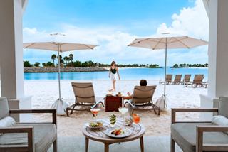 A couple relaxes with drinks and snacks under beach umbrellas at Ocean Cay by the turquoise sea | MSC Cruises