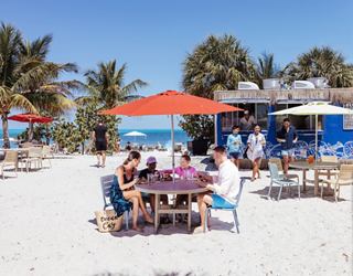 Guests enjoy dining beneath colorful umbrellas among palm trees on a sandy island | MSC Cruises