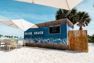 Beach shack with shaded tables and palm trees overlooking the ocean under clear sky | MSC Cruises