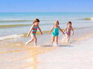 Children are playing together on a sandy beach by clear water under a bright blue sky | MSC Cruises