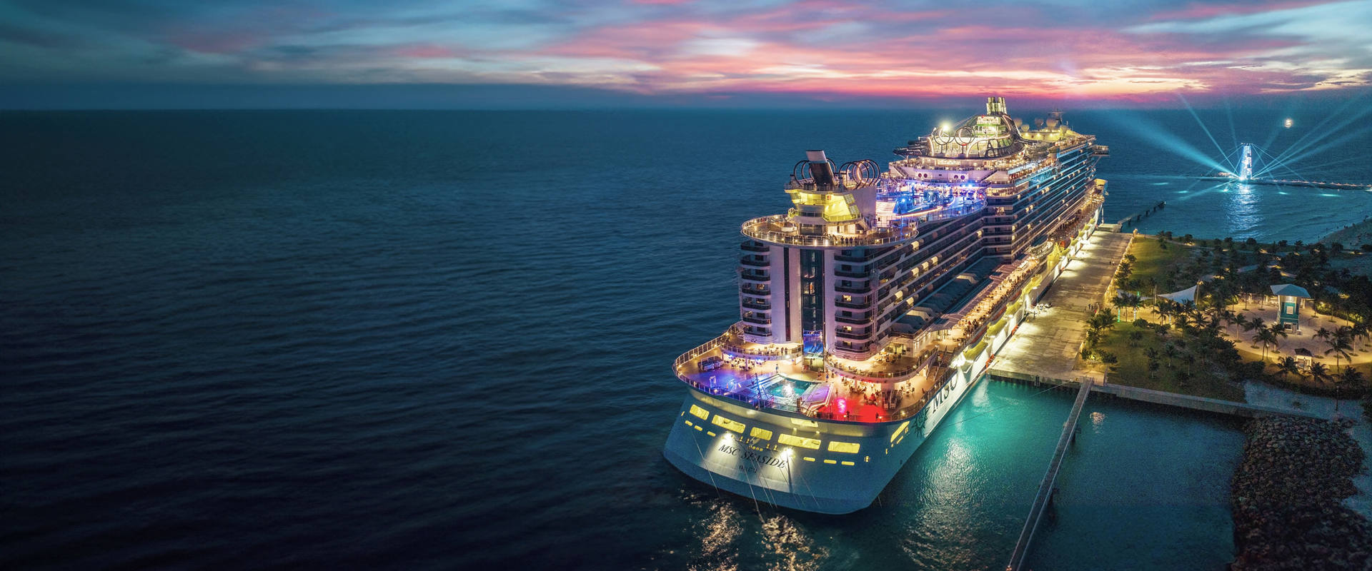 Cruise ship at Ocean Cay illuminated at night beneath a vibrant sunset sky over calm waters | MSC Cruises