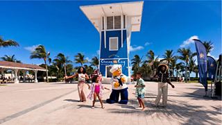 Families enjoy a sunny day by a blue tower on the beach surrounded by palm trees | MSC Cruises