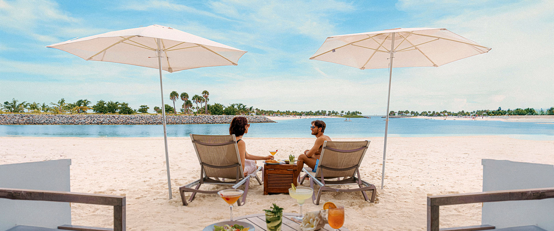 A couple relaxes under beach umbrellas with drinks and ocean views in a serene setting | MSC Cruises