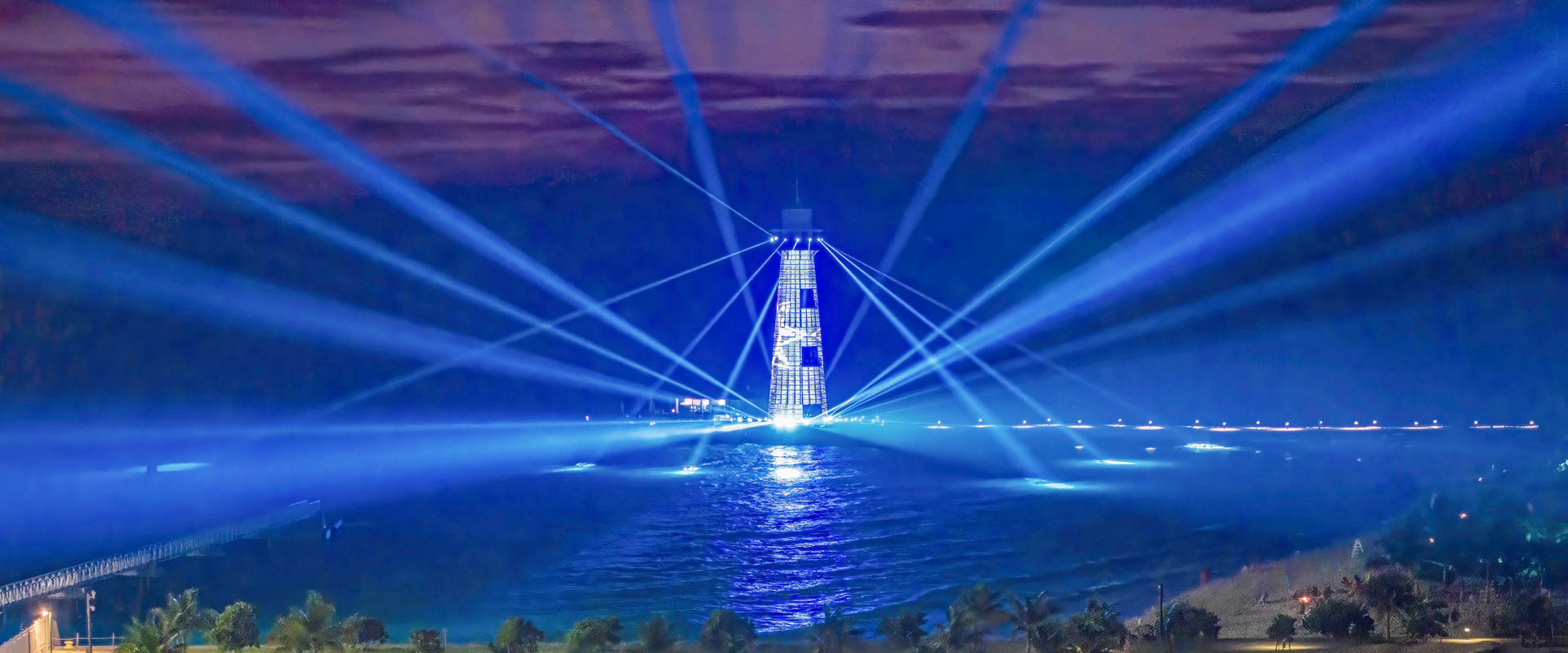 Evening lighthouse with colorful beams shining above the island and natural surroundings | MSC Cruises