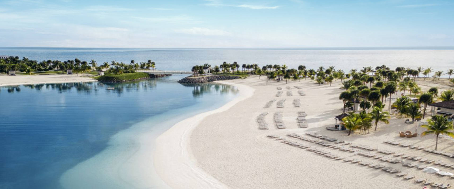White sandy beach by turquoise lagoon and green islands beneath a clear sky | MSC Cruises