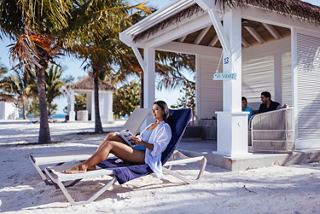 Family relaxes on sunbeds under a cabana with palm trees on the beach at Ocean Cay | MSC Cruises