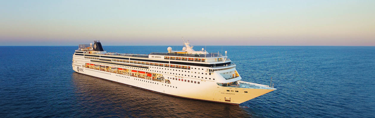 A cruise ship sails on calm blue waters, illuminated by the warm glow of sunset | MSC Cruises