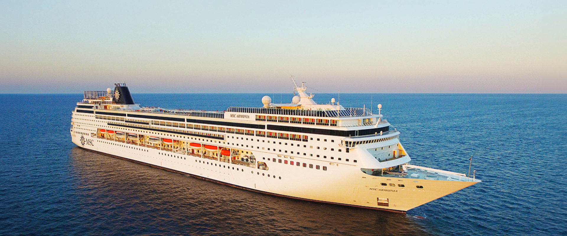 A cruise ship sails on calm blue waters, illuminated by the warm glow of sunset | MSC Cruises