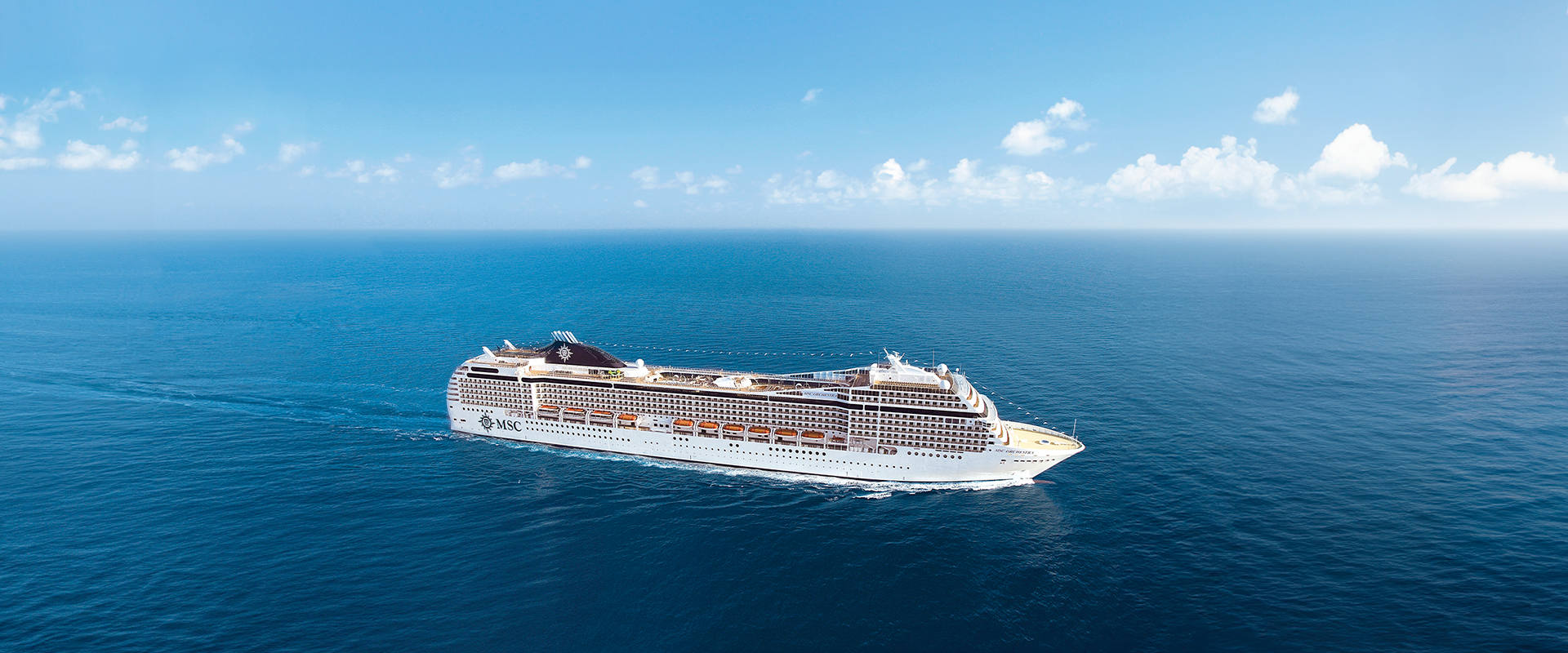A cruise ship sails across the open blue sea beneath a clear sky | MSC Cruises