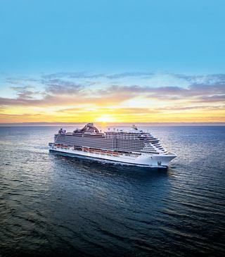 A cruise ship sails across calm waters with a sunrise and a clear sky above | MSC Cruises