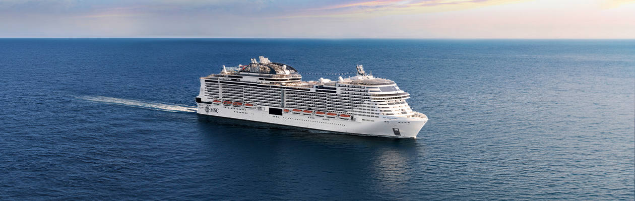 A cruise ship sails across calm blue waters beneath a vibrant sky | MSC Cruises