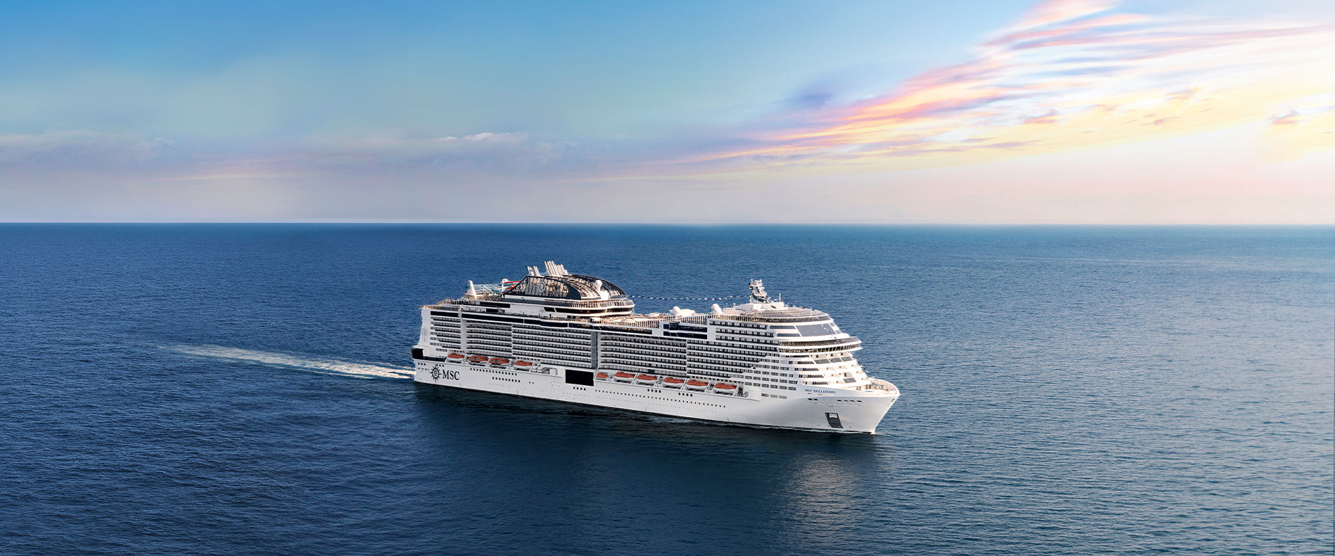 A cruise ship sails across calm blue waters beneath a vibrant sky | MSC Cruises